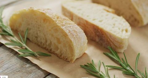 Rustic ciabatta slices sitting on parchment with fresh rosemary for food styling