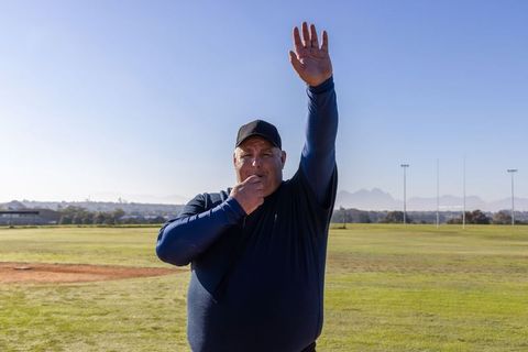Referee blowing whistle raising arm on sunny grass sports field signaling play stoppage