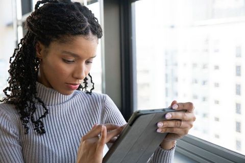 African american woman using tablet by high-rise window wearing gray turtleneck for remote work