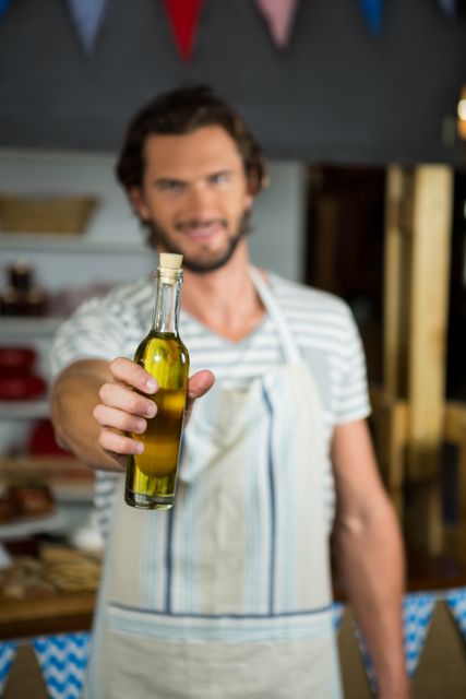 Smiling shop assistant holding a bottle of olive oil in a grocery store. Ideal for use in marketing materials for grocery stores, organic food shops, and small businesses. Can be used to promote customer service, healthy products, and local markets.