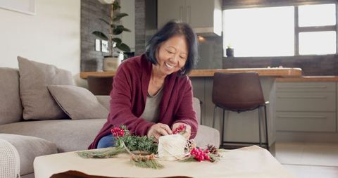 Senior woman creating festive floral arrangement with pine branches