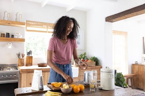 African american woman preparing fresh orange juice and fruit bowl in rustic kitchen