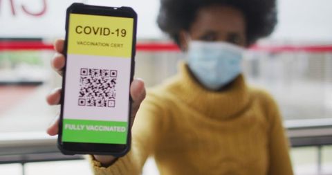 Businesswoman displaying covid-19 vaccine certificate on smartphone