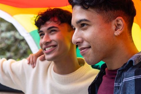 Happy Diverse Couple Under Rainbow Flag at Park Embracing Pride