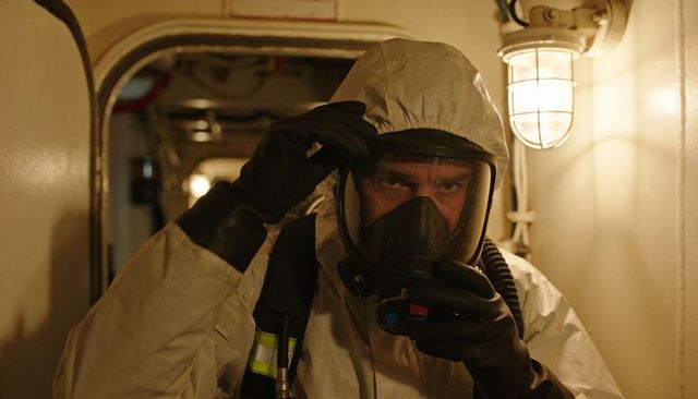 Hazmat technician adjusting respirator in narrow industrial corridor with amber light