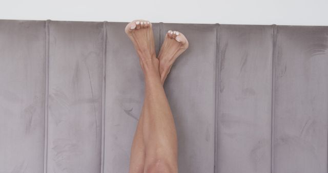 Pair of legs resting vertically against a modern, padded headboard. Ideal for wellness blogs, articles on self-care practices, or furniture advertisements highlighting stylish bedroom decor.