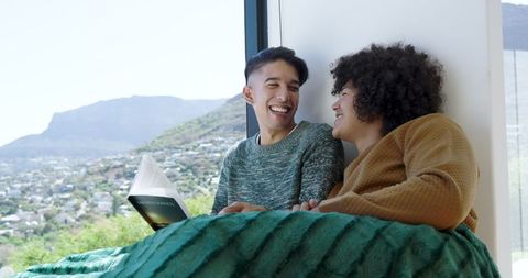 Couple Relaxing by Windowsill with Cozy Blanket and Book