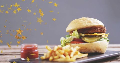 Serving gourmet burger with melted cheese, fries and ketchup on slate with gold confetti