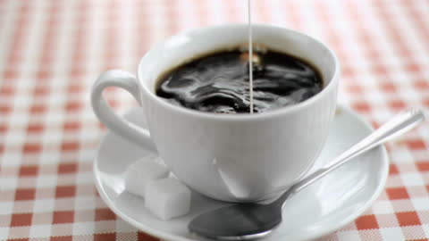 Milk Being Poured into Steaming Cup of Coffee on Checkered Table