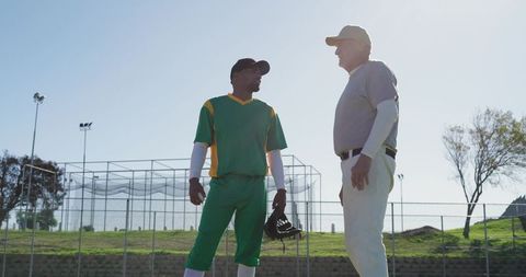 African american baseball player and senior coach discussing strategy near batting cage