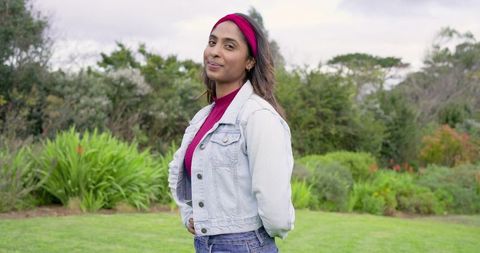 Indian woman standing in garden wearing denim jacket and magenta headband, candid portrait