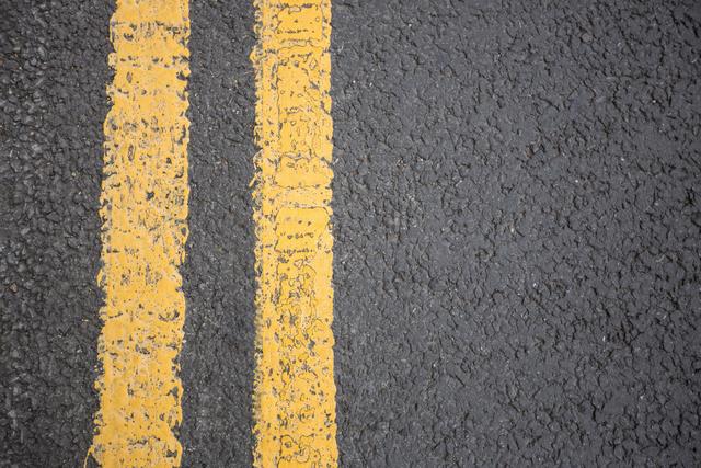 Close-up view of yellow road markings on asphalt surface. Useful for illustrating concepts related to transportation, road safety, urban infrastructure, and traffic management. Ideal for use in educational materials, presentations, and articles about road maintenance and city planning.