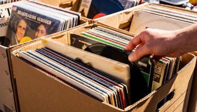 Browsing vintage vinyl records flea market hand pulling black lp from cardboard crate