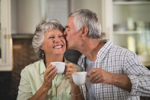 Senior man kissing wife while having coffee at home