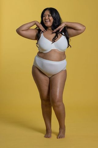 Confident plus-size woman smiling in white lingerie against yellow background