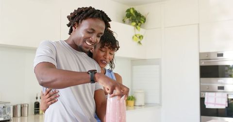 African american couple preparing pink smoothie in modern kitchen for healthy lifestyle