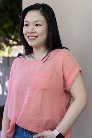 Asian woman smiling standing outdoors in coral blouse and denim jeans wearing smartwatch