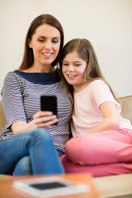 Mother and daughter using mobile in living room at home
