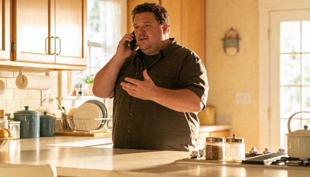 Man talking on phone in sunlit cozy kitchen gesturing at island with spices and stovetop