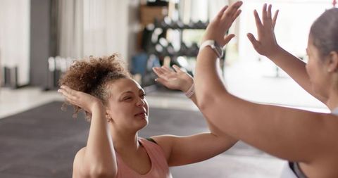 Two women high-fiving after workout in sunlit gym studio boosting teamwork and fitness motivation