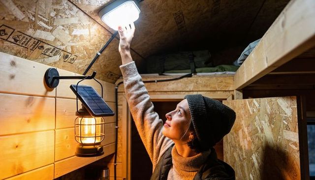 Reaching woman installing led light in off-grid tiny cabin with solar lantern
