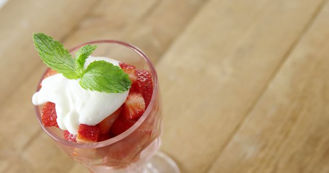This image shows a refreshing strawberry dessert served in a glass cup. The dessert is topped with whipped cream and garnished with a fresh mint leaf. Perfect for use in culinary blogs, recipe sites, healthy eating promotions, summer-themed advertisements, and dessert menus.