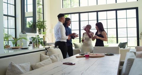 Diverse friends chatting in modern living dining space with large windows and plants