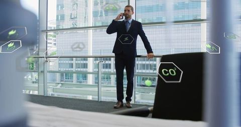 Executive talking on smartphone in modern glass atrium with ar sustainability icons