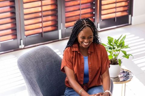 Smiling african woman relaxing in sunlit modern living room with gray armchair and plant