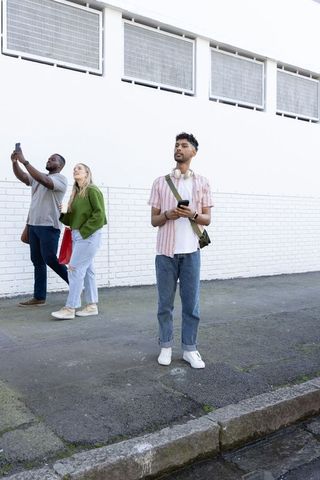 Multiracial friends walking urban sidewalk using smartphones, minimalist street life scene