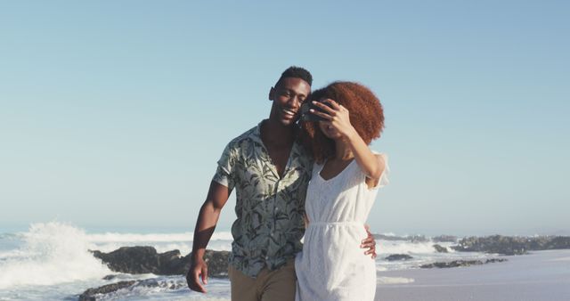 Happy diverse couple embracing and walking on sunny beach by the sea. Summer, free time, relaxation, romance and vacations.