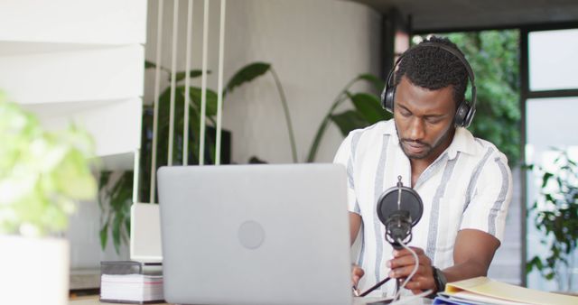Man concentrating while recording a podcast using a microphone and wearing headphones. Ideal for concepts related to podcasting, content creation, remote work, communication, technology in modern workspaces. Useful for illustrating articles on home offices, online content generation, and professional broadcasting.