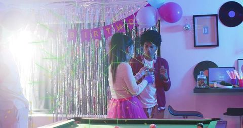 Young adults chatting at neon birthday pool table party with disco fringe and balloons