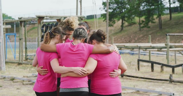Happy caucasian female friends in pink t shirts embracing in huddle after cross training at bootcamp. Female fitness, challenge, friendship and healthy lifestyle.