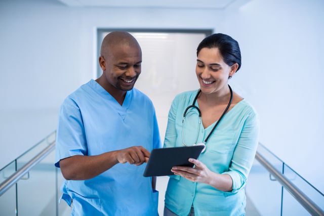 Doctors are collaborating and discussing patient care using a digital tablet in a hospital corridor. This image can be used to depict modern healthcare practices, teamwork among medical professionals, and the integration of technology in healthcare settings. Ideal for use in medical websites, healthcare blogs, and promotional materials for hospitals and clinics.