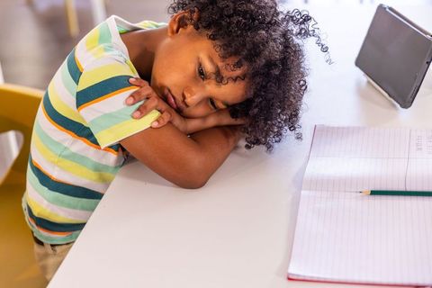 African american boy resting head on desk feeling tired during homework with tablet and notebook