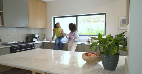 Diverse women chatting over coffee at modern kitchen island, bright casual lifestyle