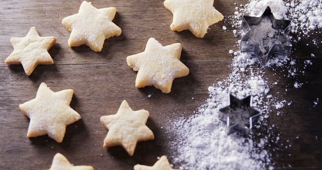 Star-shaped sugar cookies dusted with powdered sugar placed on a wooden table beside metal star-shaped cookie cutters and sprinkled flour. Perfect for use in holiday baking articles, confectionery blogs, festive recipe books, or food-related social media posts showcasing homemade sweet treats.