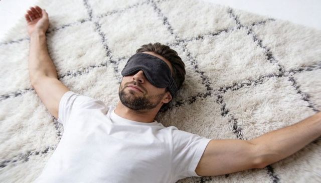 Bearded man resting with sleep mask on cream shag rug with diamond pattern