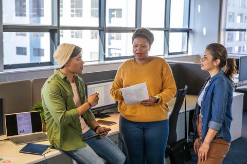 Diverse team discussing project in modern open-plan office with laptop, tablet, documents