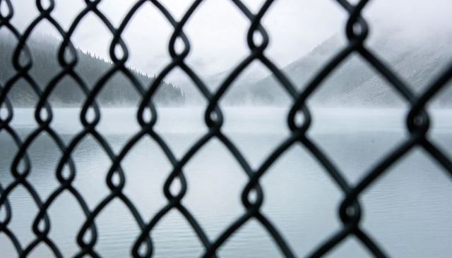 Chain-link fence framing misty mountain lake and forested ridges