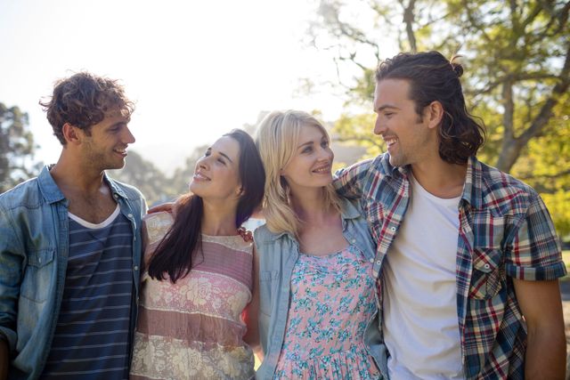 Group of friends standing close together in a park, enjoying a sunny day. They are smiling and looking at each other, dressed in casual summer clothes. Ideal for use in advertisements, social media posts, and articles about friendship, outdoor activities, and lifestyle.