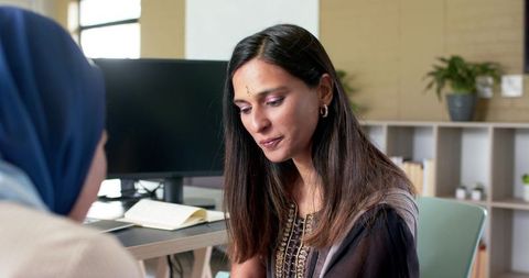 Indian women colleagues collaborating at modern office desk wearing hijab and ethnic kurta