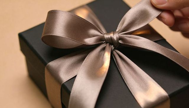 Hand Adjusting Taupe Satin Bow on Matte Black Gift Box Closeup Luxury Gift Wrapping Detail
