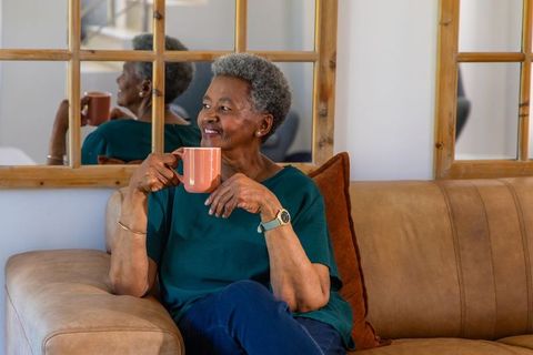 Senior black woman relaxing on sofa with coffee mug, cozy minimalist home lifestyle
