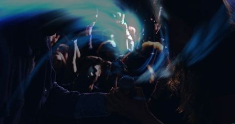 Female singer grabbing microphone from denim jacket fan amid moody blue green concert haze