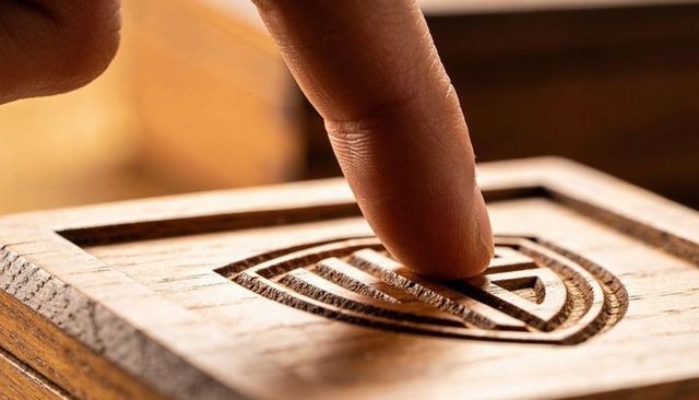 Pressing fingertip into carved wood block revealing concentric geometric grooves