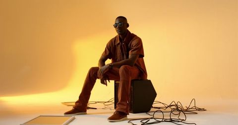 Stylish musician sitting on amplifier in studio with cables around