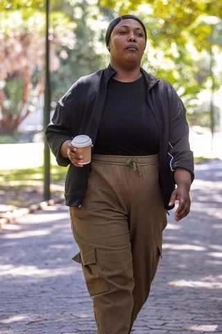African american woman walking with coffee on park path casual urban lifestyle portrait