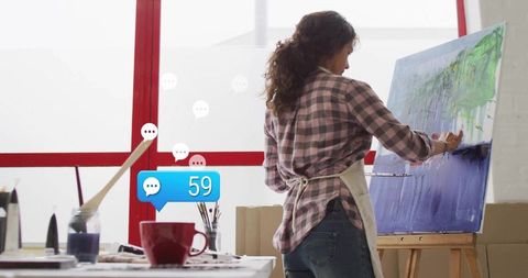 Female artist painting canvas in sunlit studio with digital interaction